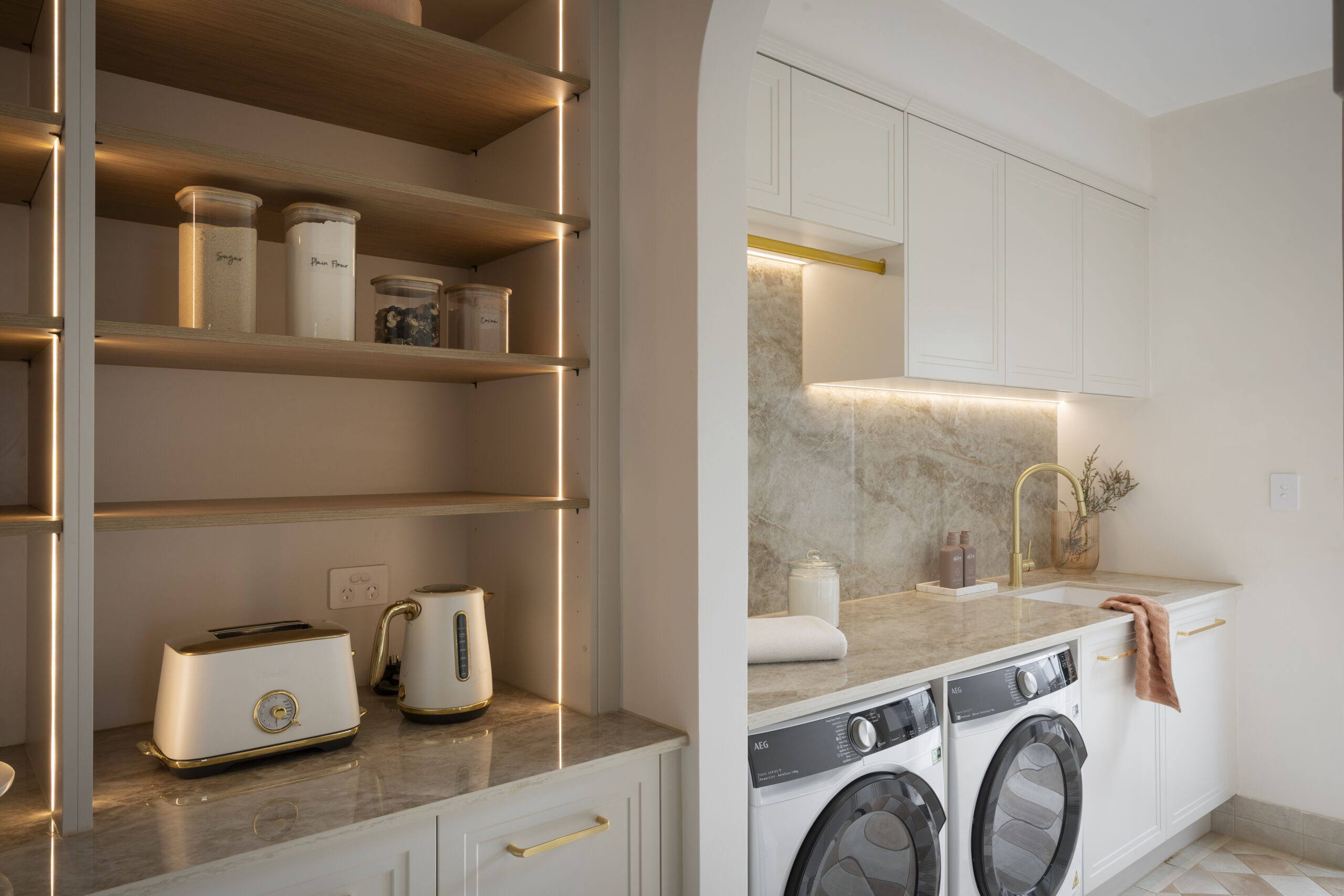 H2 HAN & CAN Laundry MA121 White shaker-style laundry with marble-look benchtop, gold tapware and side-by-side washer and dryer