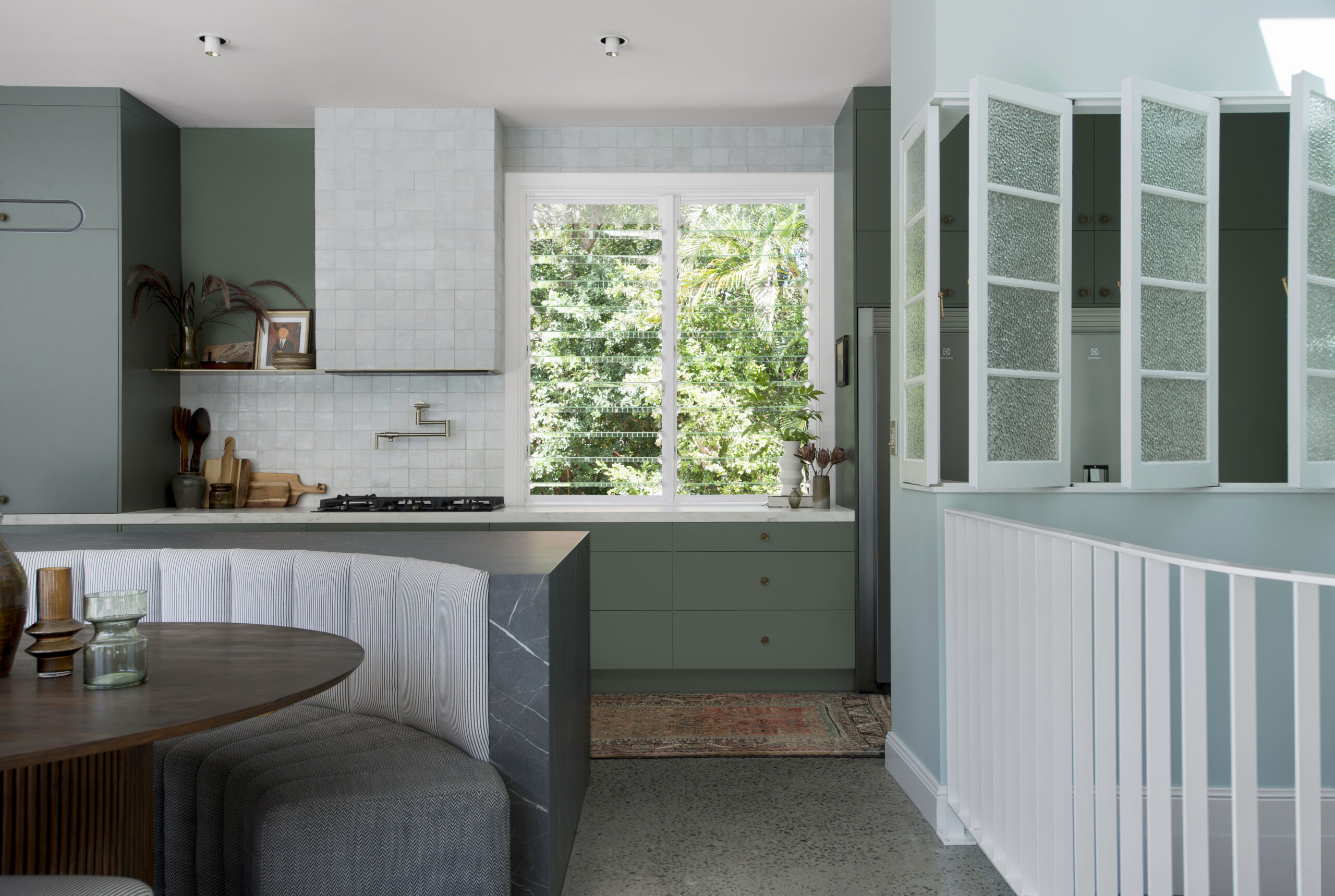 Modern family kitchen with green cabinetry, dining nook and a view out to the garden.