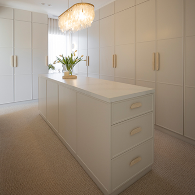 White walk in wardrobe with shaker style doors, gold handles and a large island bench