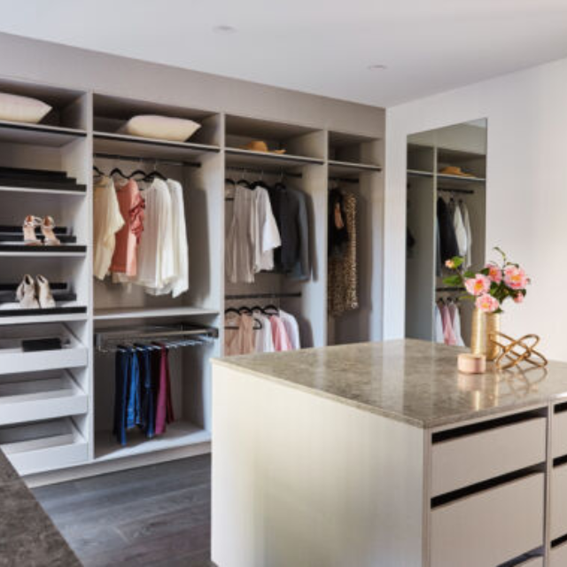 Large open walk in wardrobe with open shelving and an island bench