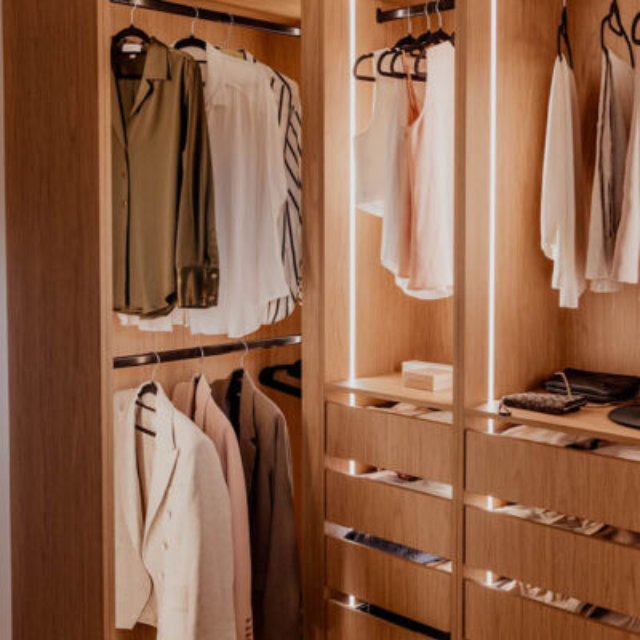 Close up of hanging space in a timber-look wardrobe in wardrobe with vertical strip lighting illuminating clothing