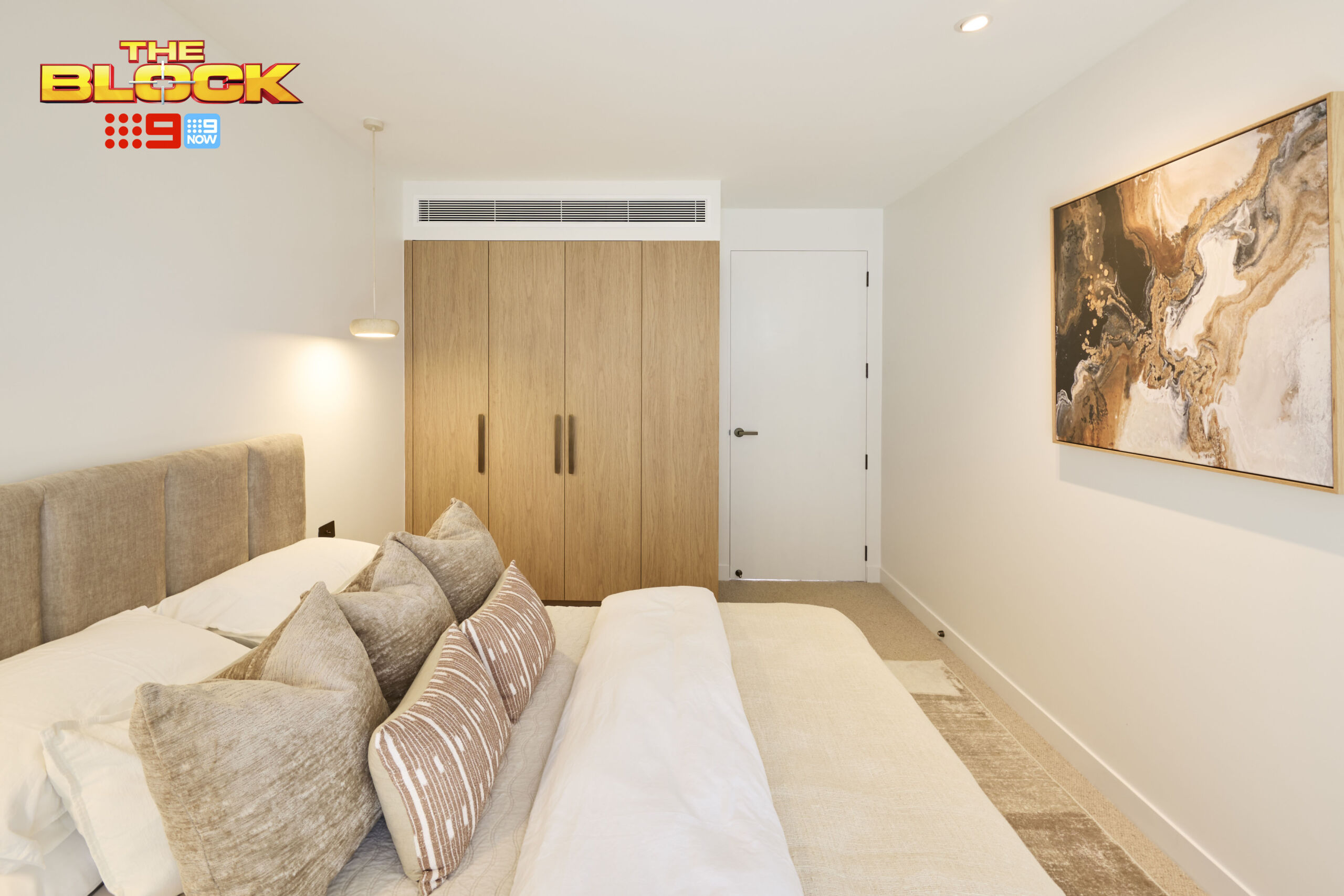 Pale timber-look four-door wardrobe in a modern guest bedroom with a soft fabric bedhead, linen bedding, and neutral pillows.