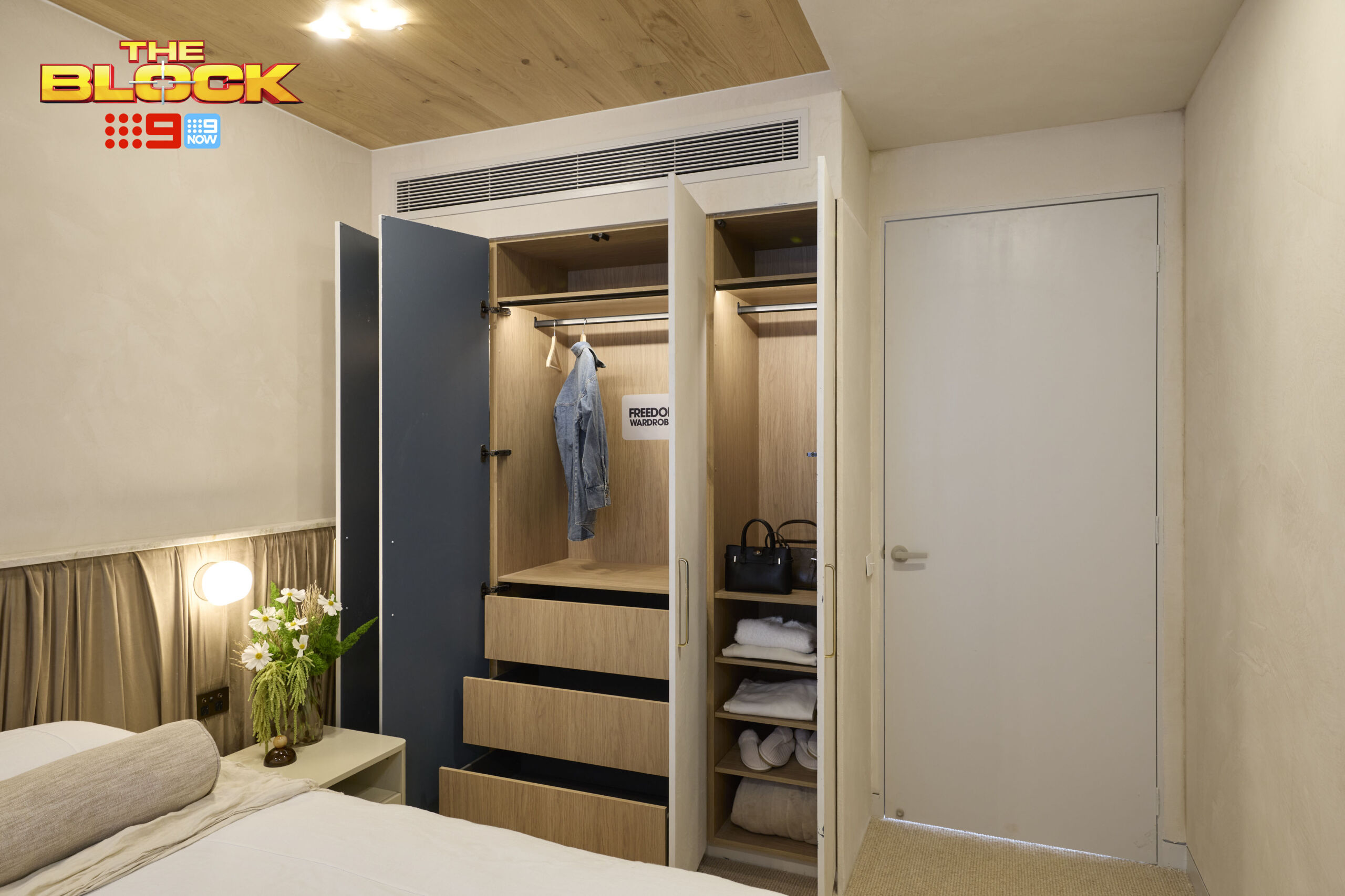 Built-in wardrobe with timber-look interiors, showcasing organised storage with hanging rails, drawers, and open shelving.