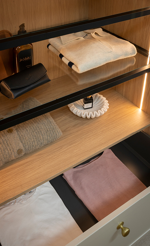 Glass-front wardrobe shelving with integrated lighting and folded clothing