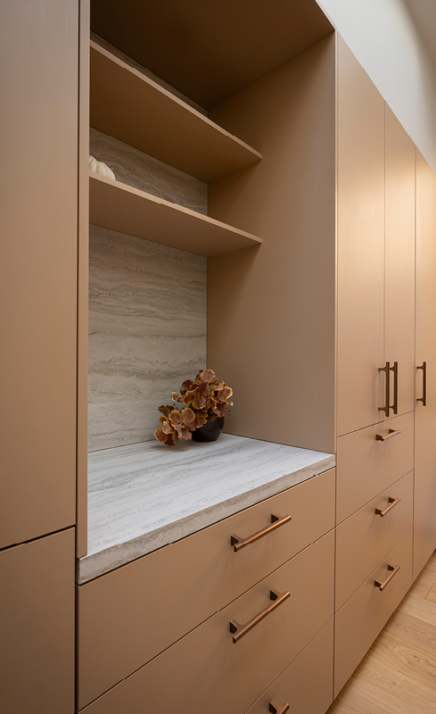Warm wardrobe cabinetry with open shelving, stone benchtop and bronze handles