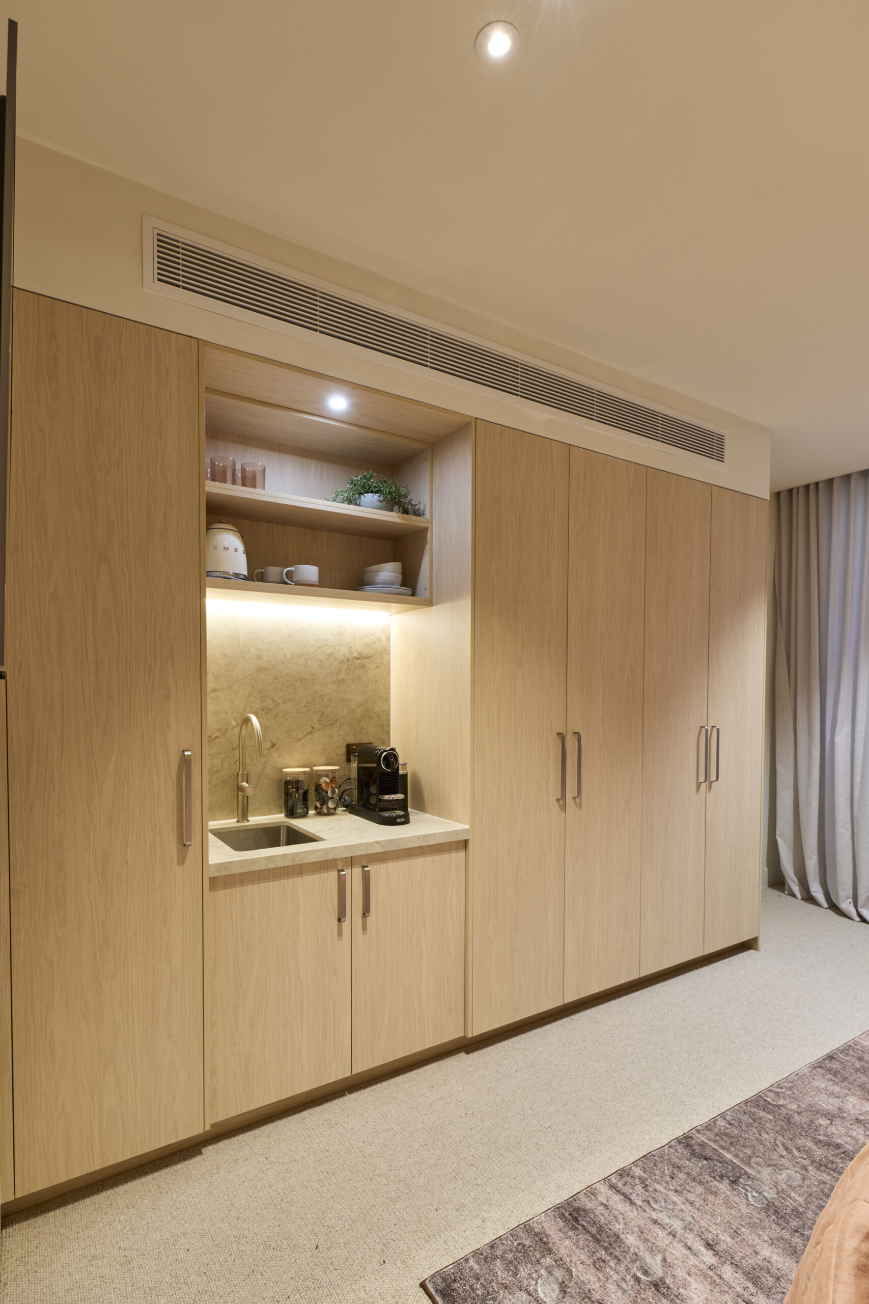 H4 RM6 GUEST SUITE BEDROOM & ENSUITE Courtney and Sev-080 Timber look built in wardrobe with bar area with a sink and tap and coffee machine and kettle.
