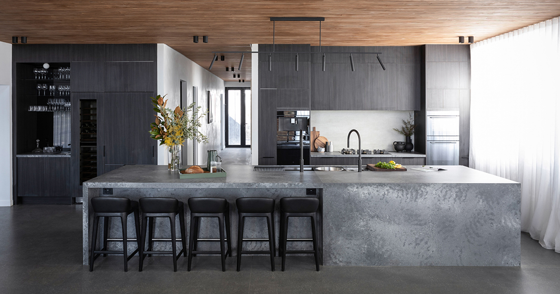 industrial-oct26-2 Modern industrial kitchen with dark timber-look cabinetry, concrete-look waterfall island and black track lighting