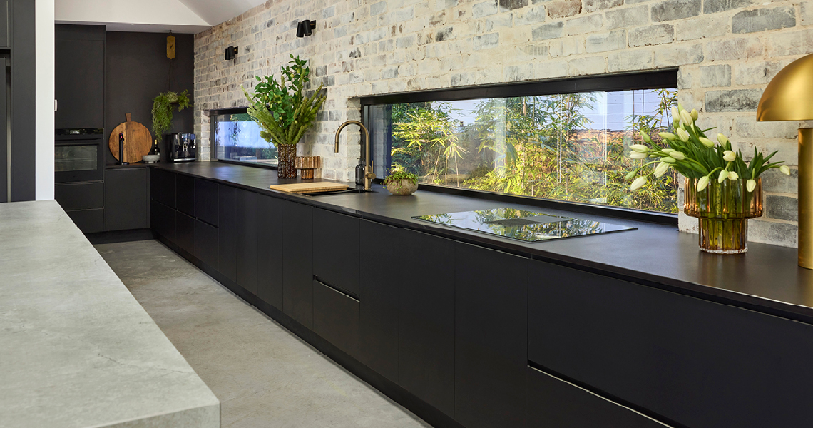 industrial-oct26-3 Black kitchen cabinetry and benchtop against an exposed brick wall with a window splashback